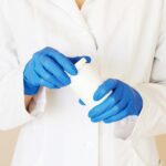 A person in a lab coat and gloves holding a pill bottle