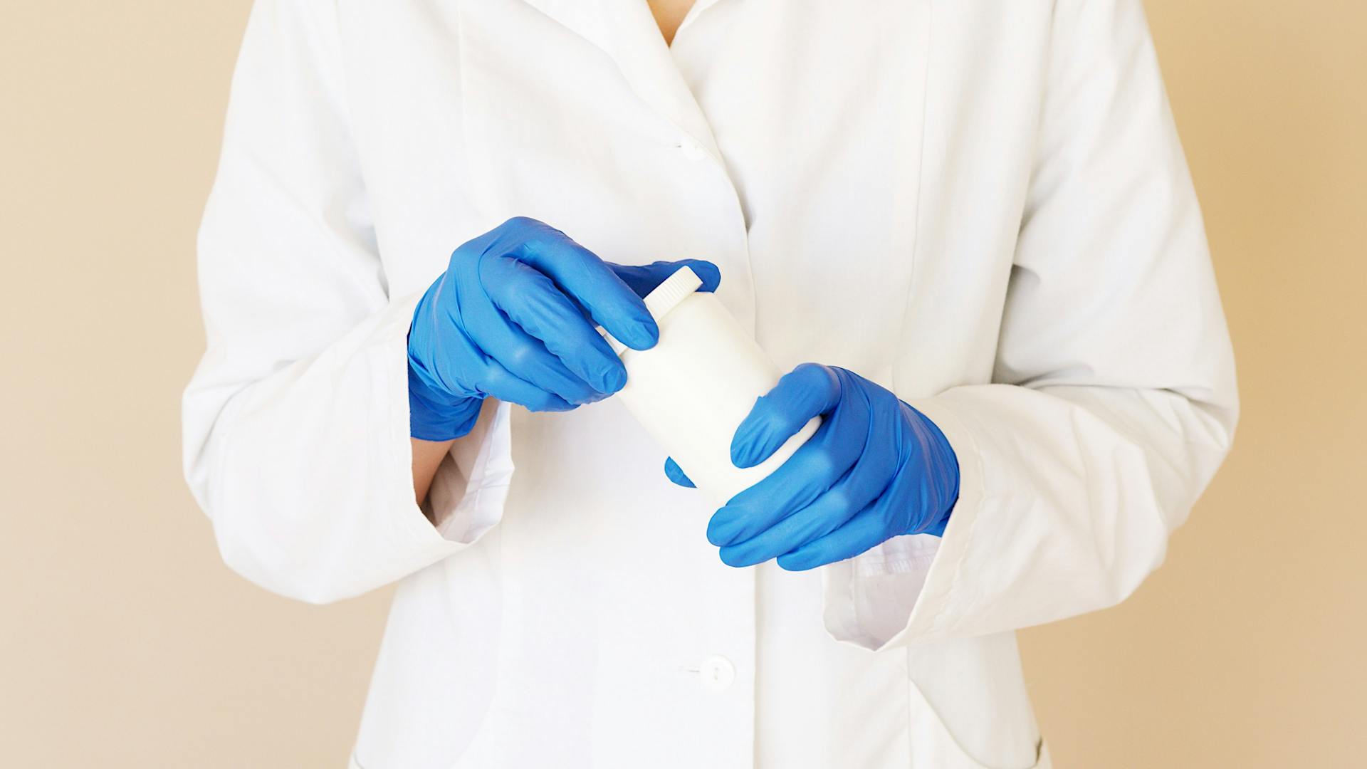 A person in a lab coat and gloves holding a pill bottle