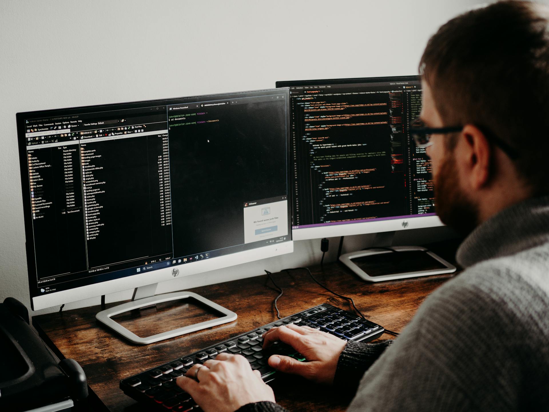 A man does coding on a computer with two monitors.