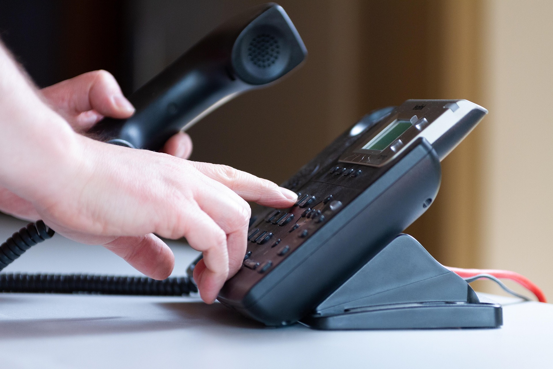 A person dialing a number on a landline phone.