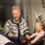 Priscilla, a young girl in a mobility device, uses a switch on her tray, as her mother Ashley holds her hand.