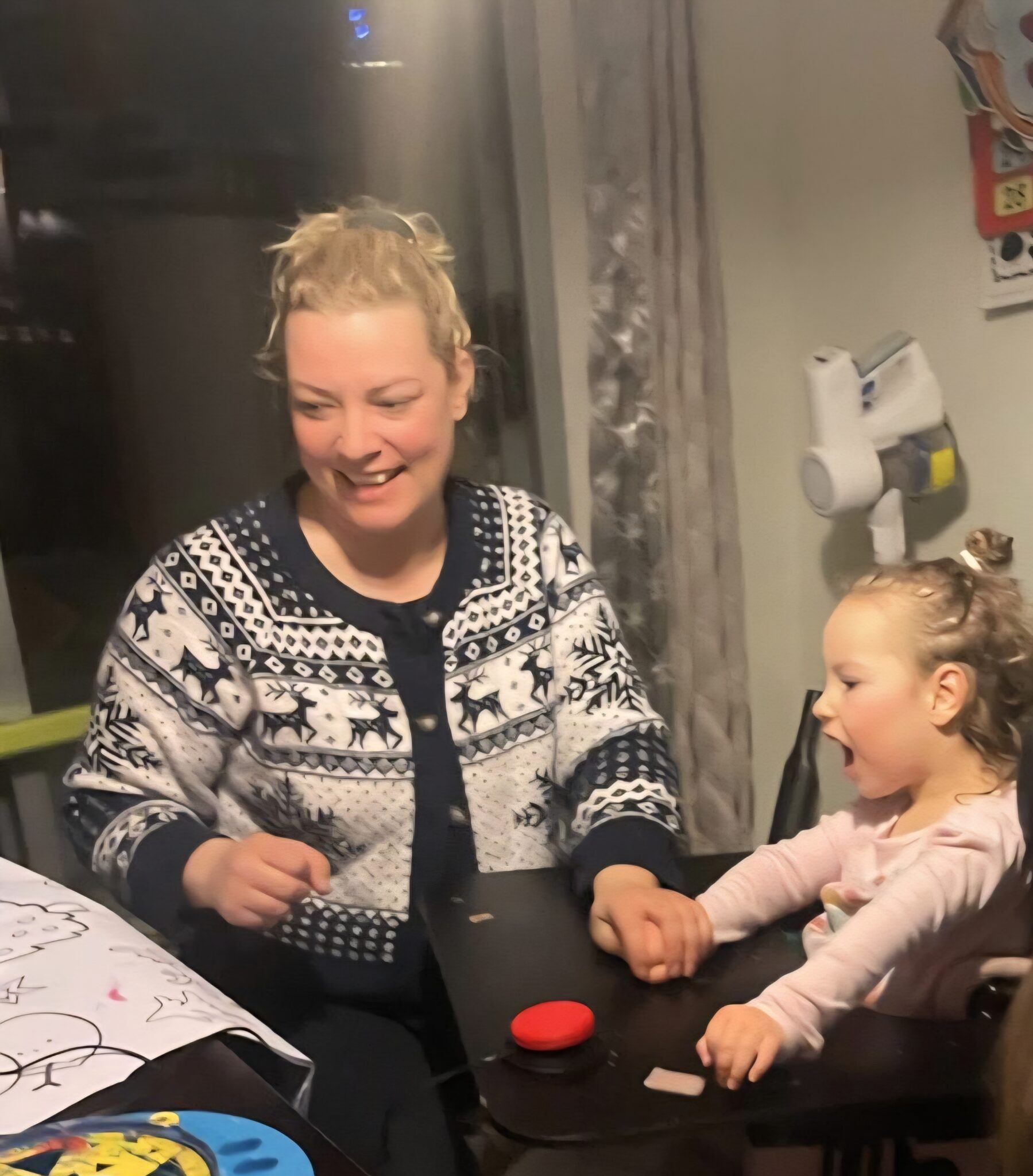 Priscilla, a young girl in a mobility device, uses a switch on her tray, as her mother Ashley holds her hand.