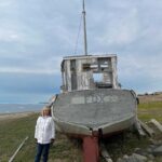 Susan standing near a beached boat on a beach.
