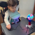 Sandro, in a wheelchair, playing a switch-adapted toy on his lap tray.