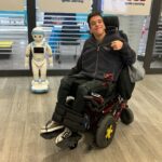 Nico in a wheelchair, in front of signs for the Durham District School Board.