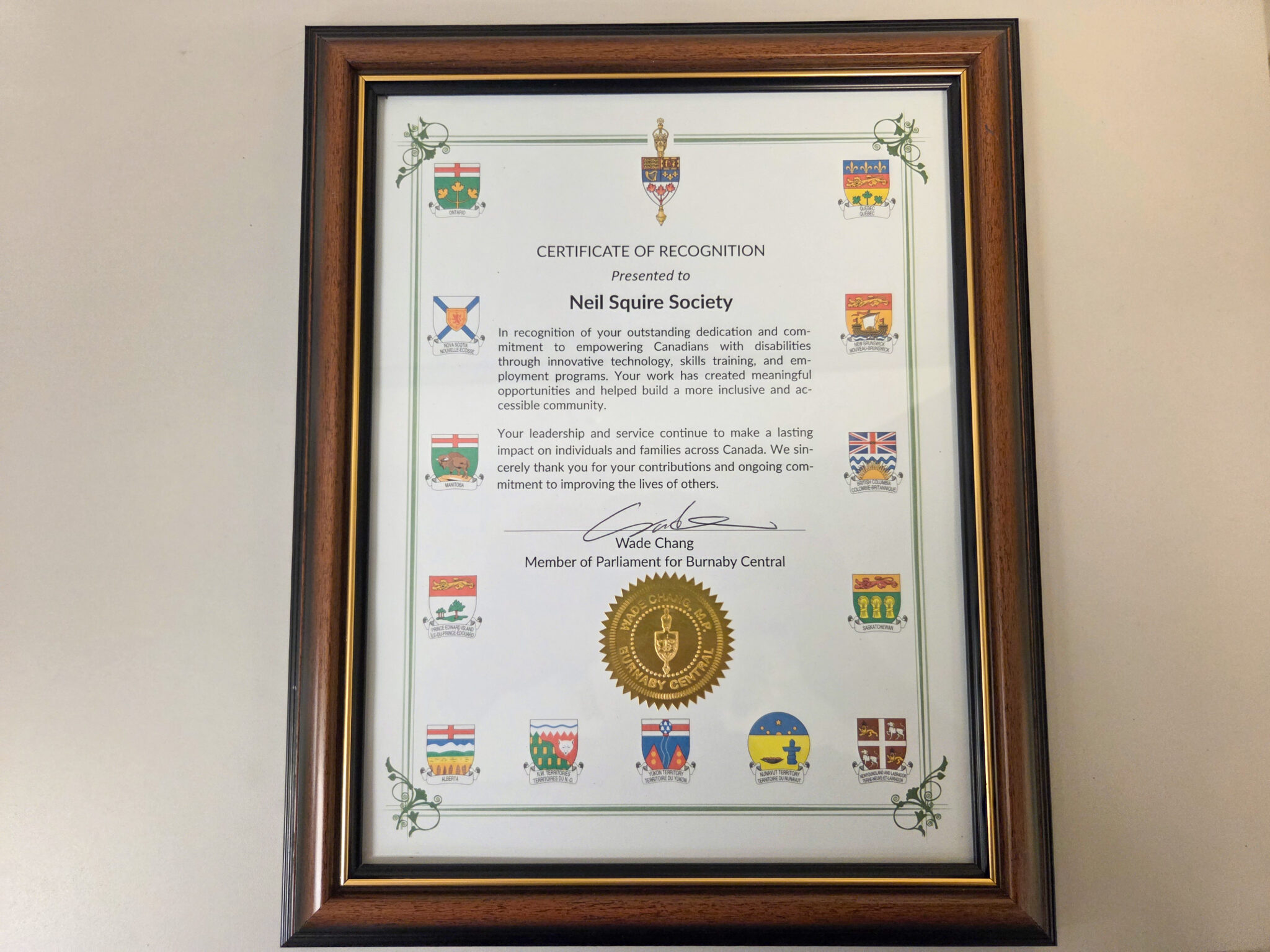 The certificate reads: "Certificate of Recognition presented to Neil Squire Society. In recognition of your outstanding dedication to empowering Canadians with disabilities through innovative technology, skills training,, and employment programs. Your work has created meaningful opportunities and helped build a more inclusive and accessible community. Your leadership and service continue to make a lasting impact on individuals and families across Canada. We sincerely thank you for your contributions and ongoing commitment to improving the lives of others." Signed by Wade Chang, Member of Parliament for Burnaby Central.