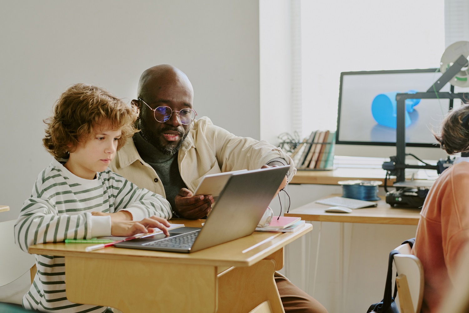 A teacher helps a student using a laptop in a classroom.