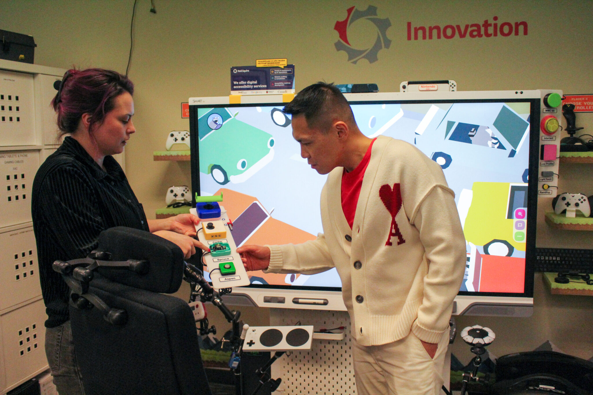 MMC BC Outreach & Operations Coordinator Kris Stirling demonstrates an adaptive controller for adaptive gaming to MP Wade Chang.