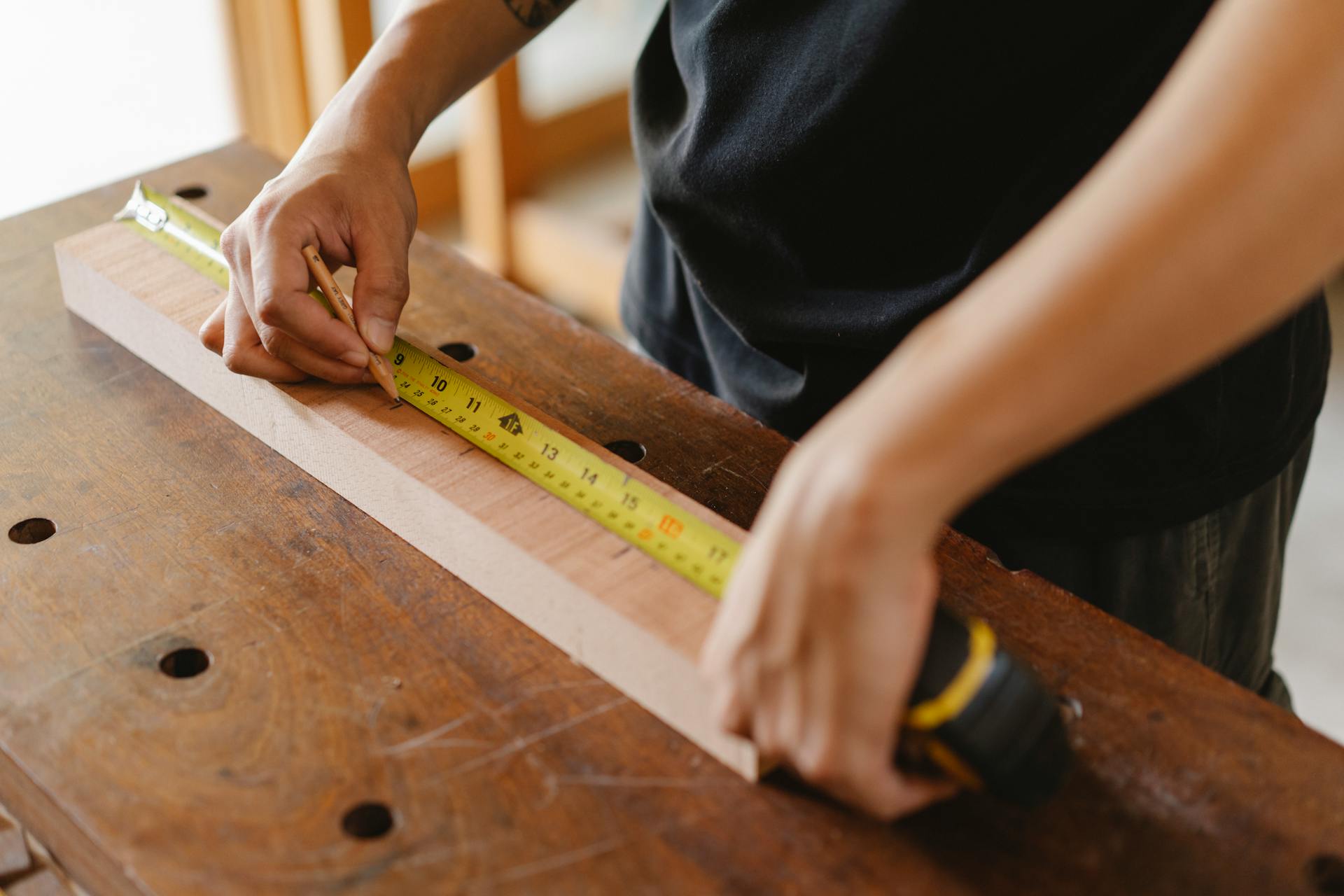 A person measures a board of wood with a tape measurer.