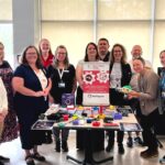 Clinicians at the Nova Scotia Rehabilitation and Arthritis Centre and MMC staff pose together for a photo next to a table with an MMC banner and adaptive gaming devices.