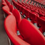 Curved rows of empty bright red stadium seats stretching into the distance in a large arena.