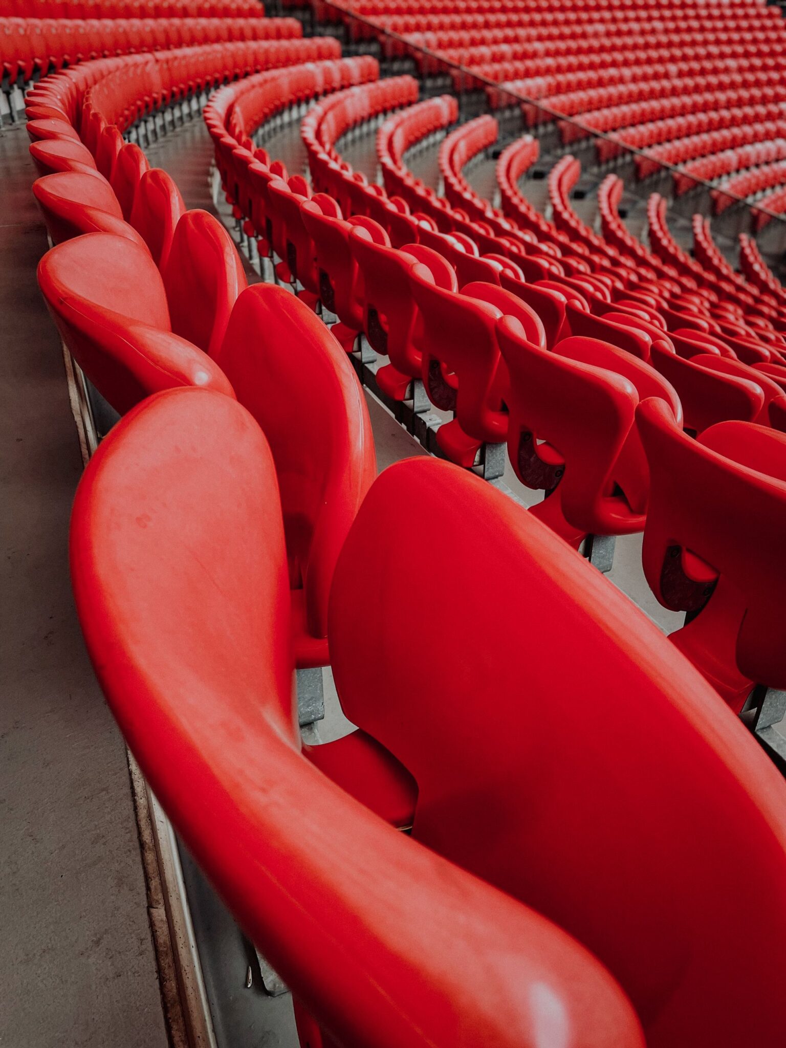 Curved rows of empty bright red stadium seats stretching into the distance in a large arena.