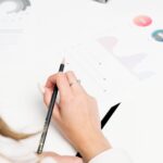 Person holding a pencil and analyzing printed charts and graphs on a white desk.