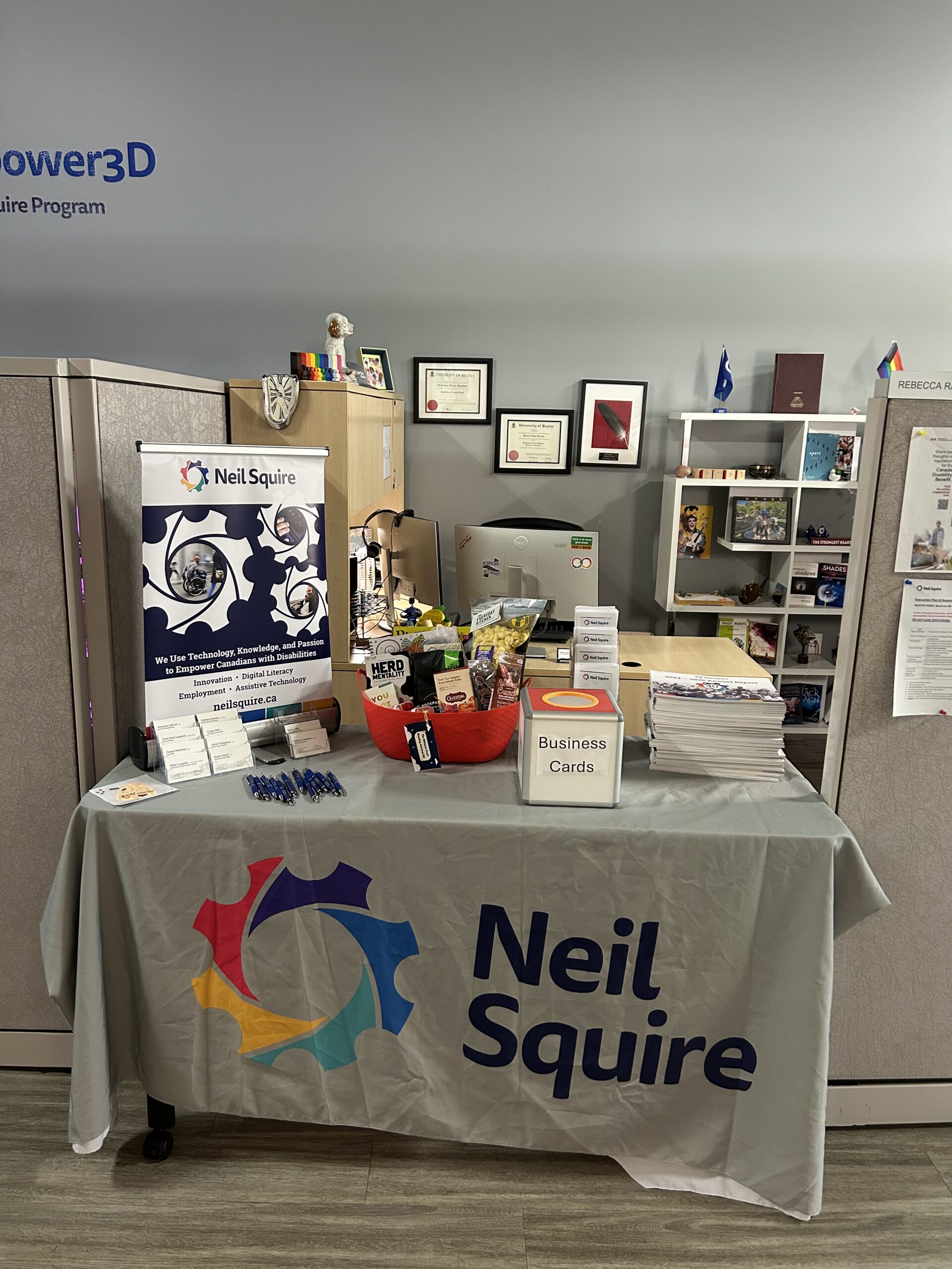 Neil Squire information booth with brochures, business cards, pens, and promotional materials on a table in an office cubicle.