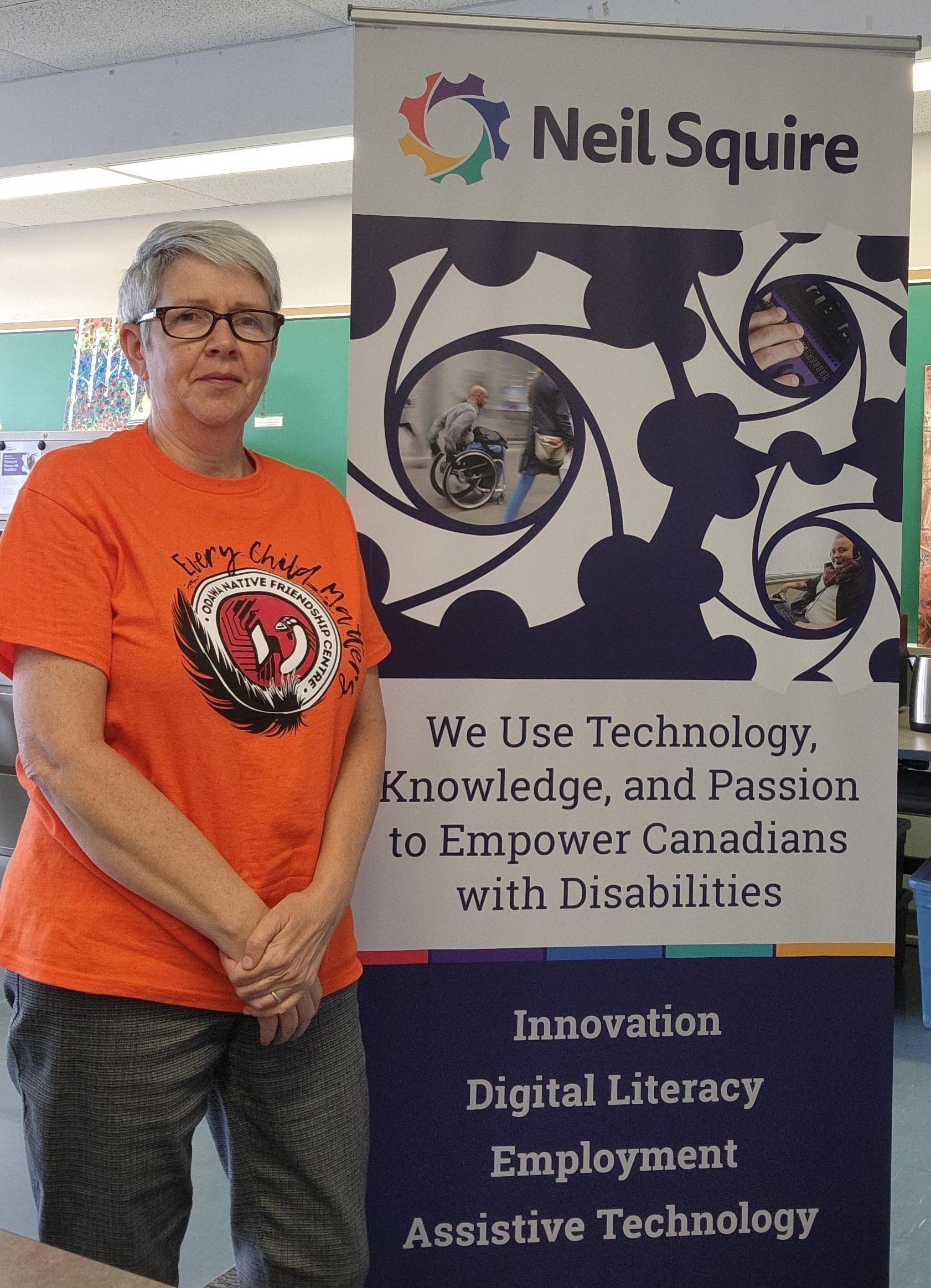 Cheryl from our Ottawa office wearing an orange shirt in front of the Neil Squire sign.