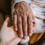 An elderly hand resting gently on a younger person's open palm, symbolizing care and connection.