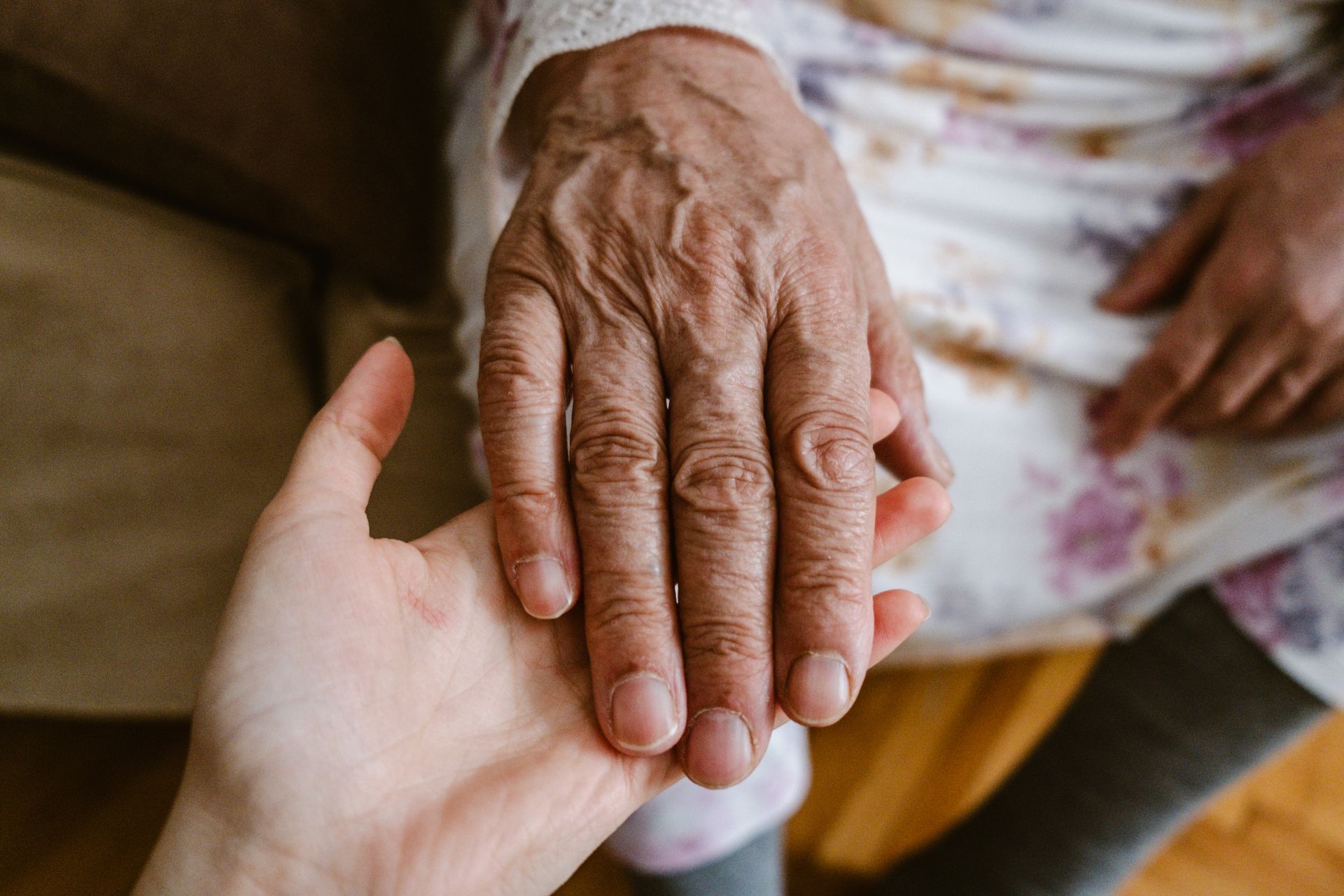An elderly hand resting gently on a younger person's open palm, symbolizing care and connection.