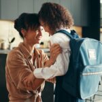 Mother and daughter sharing a joyful moment in a modern kitchen as the child prepares to leave for school with a blue backpack.