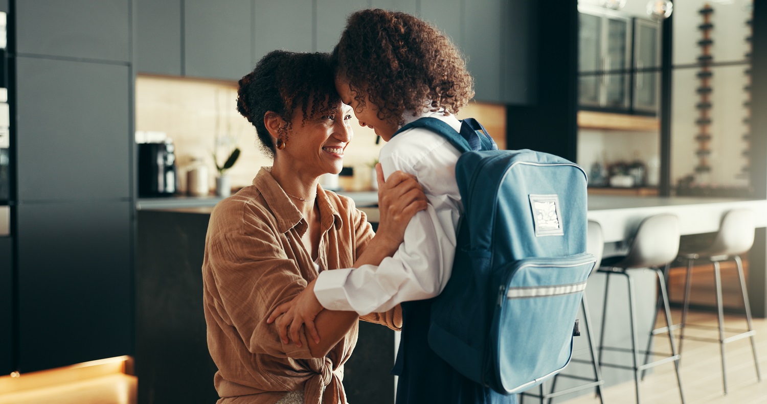 Mother and daughter sharing a joyful moment in a modern kitchen as the child prepares to leave for school with a blue backpack.