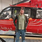 Karl standing smiling in front of the red STARS helicopter inside the hangar.