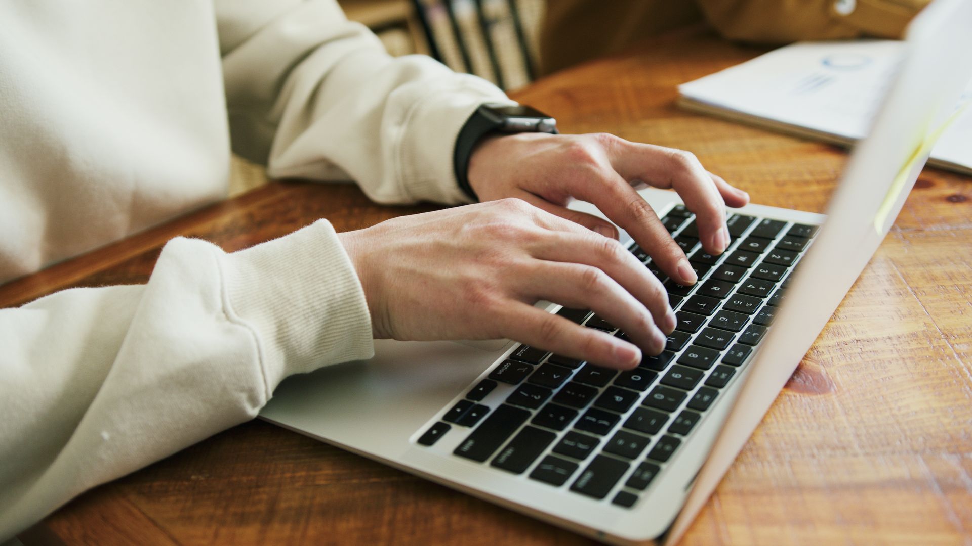 Person typing on a laptop keyboard at a wooden desk.