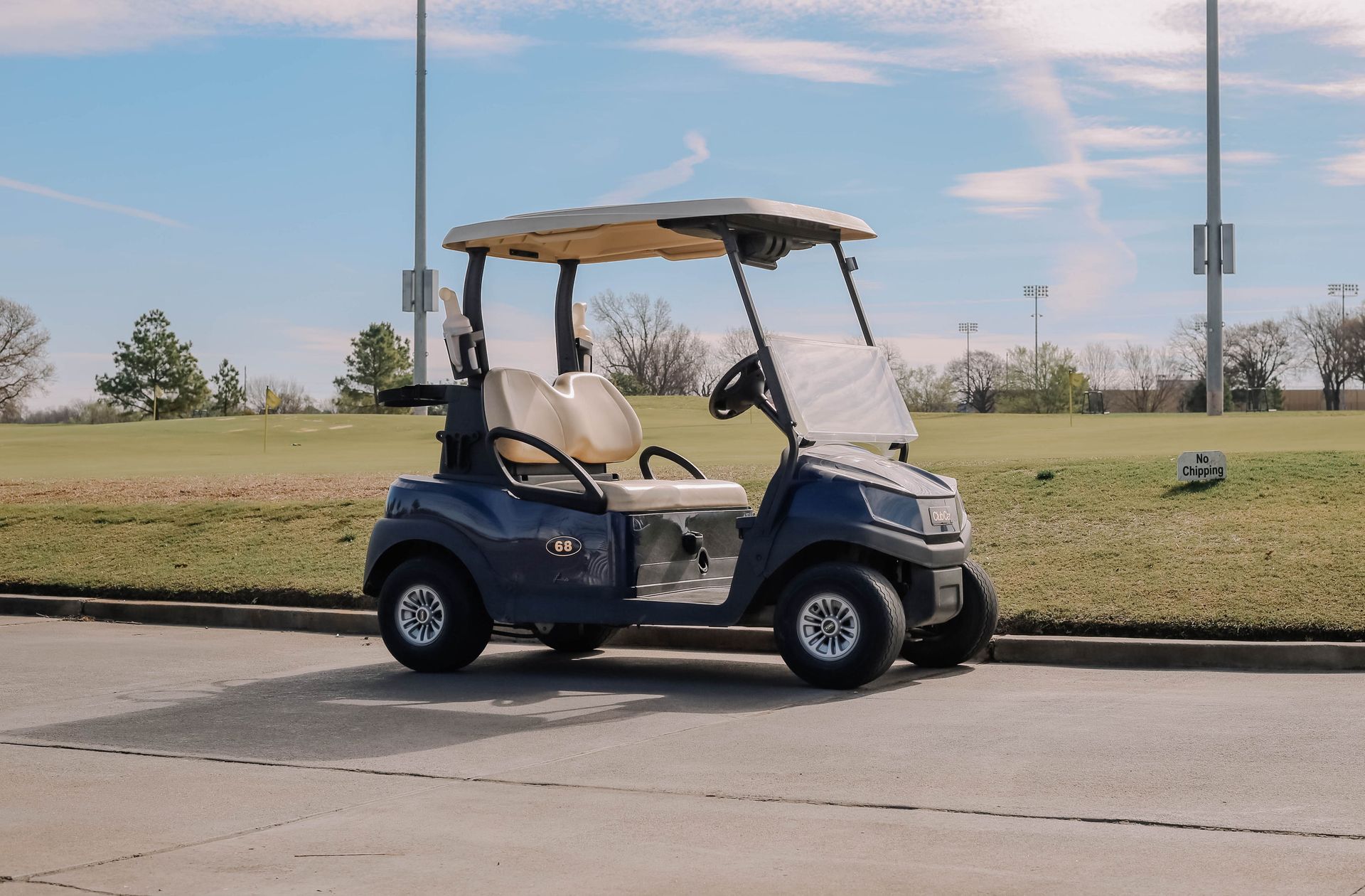 Golf cart parked on a paved path next to a grassy golf course under a partly cloudy sky.