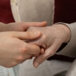 A younger person gently holding the hand of an elderly individual, conveying care and support.